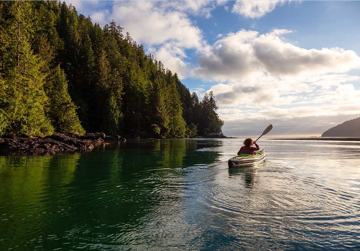 A woman kayaks along the rugged shoreline of Vancouver Island
