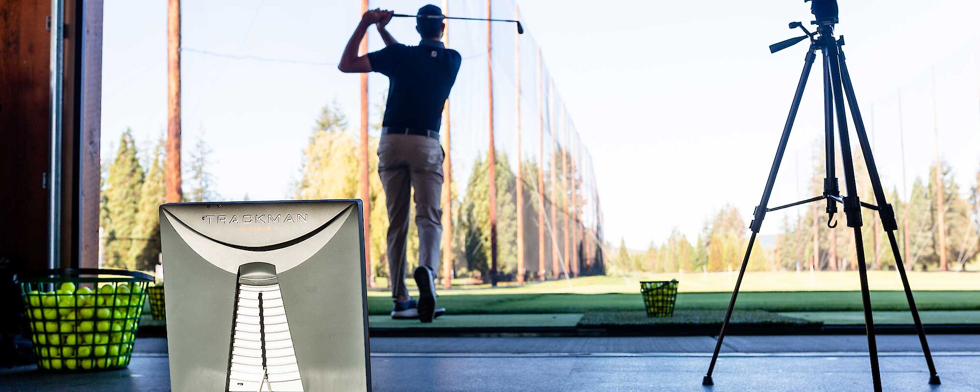 A golf pro has his arms up with his club after a full swing with a Trackman computer in the foreground analyzing his swing.