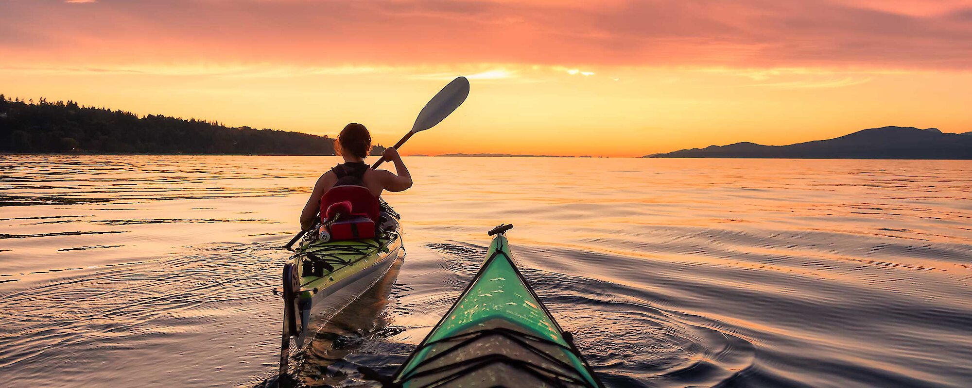 Two people kayak into the sunset in the waters around Campbell River