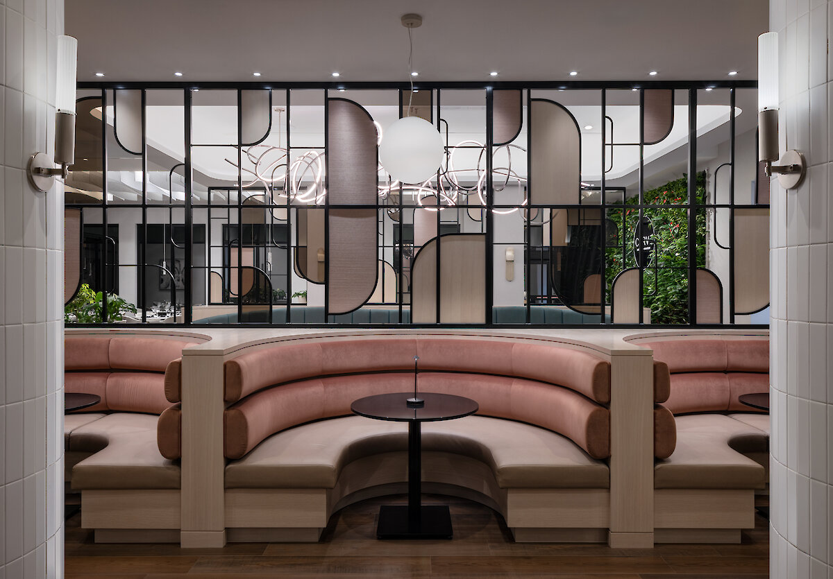 A glimpse inside the neutral coloured restaurant with tables for 4 with modern, c-shaped dining chairs, and a living wall.