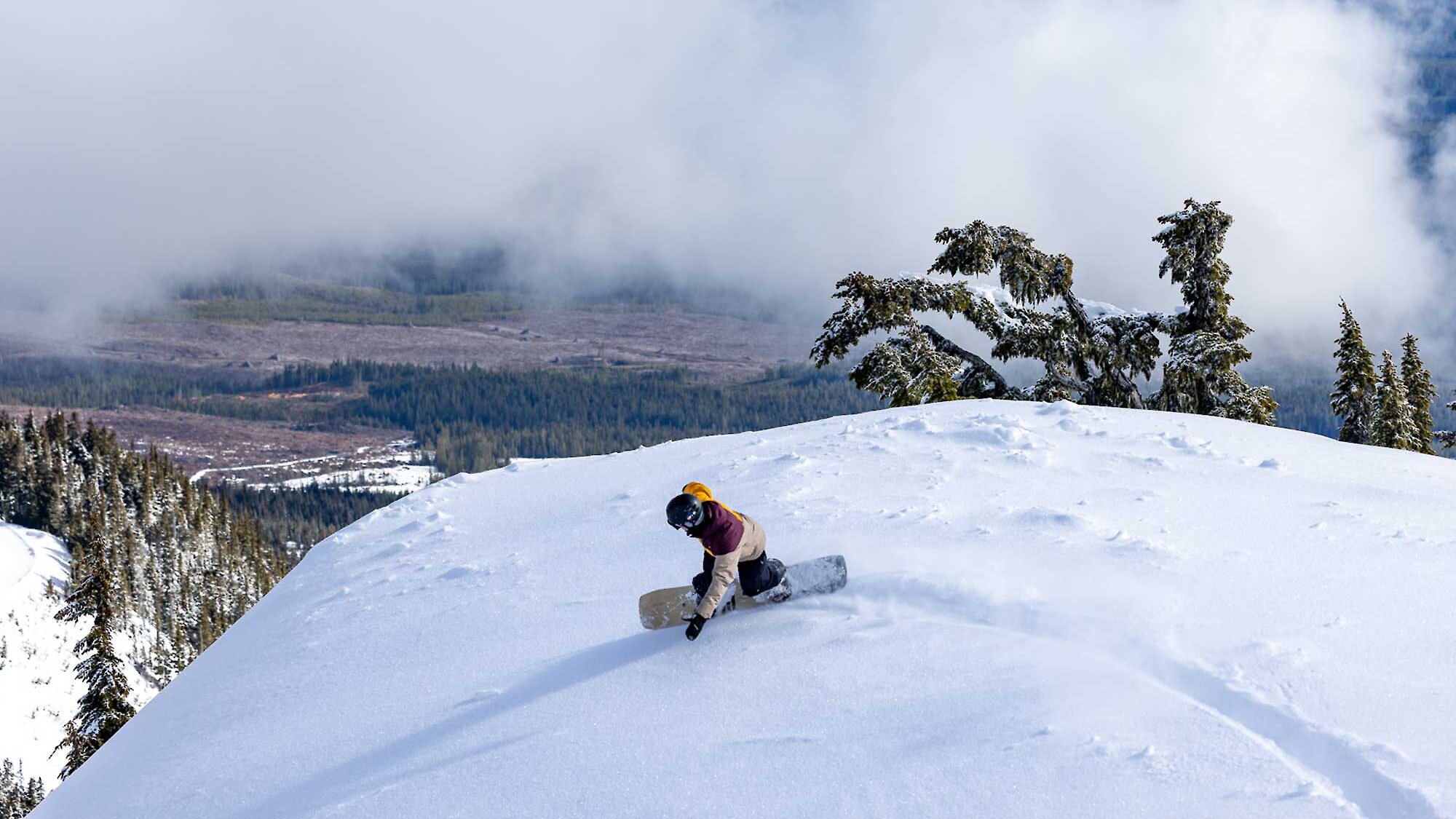 A snowboarder heads down Mount Washington on a blue and cloudy sky, with a clear view of the Comox Valley below.