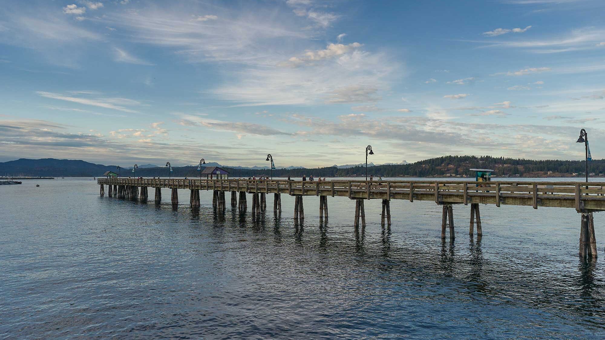 The Campbell River Pier stretches out along the blue sky and water with Quadra Island in the background.